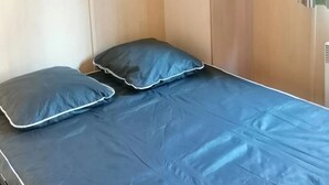 Une petite pièce comprenant un lit, deux oreillers, une armoire et une étagère.