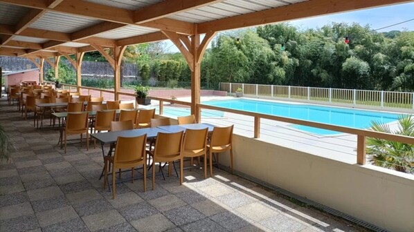 Eine Terrasse im Freien mit Tischen und Stühlen, ein Schwimmbad und Blick auf Bäume.