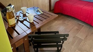 Tunnelmallinen huone, jossa on puinen pöytä, penkki, punaisella peitolla varustettu sänky ja kaksi ikkunaa.