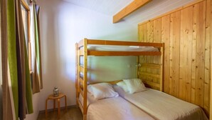 A bunk bed room with a wooden headboard, a small wooden stool, and a window with curtains.