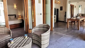 A room with a bed, wicker chairs, a small table with mugs, and a dining area with a wooden table and chairs. - Private House! 2' to the beach, AC, Wi-Fi, Pool (Malpais)