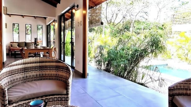 A covered outdoor area with wicker furniture, a pool, and lush greenery. - Private House! 2' to the beach, AC, Wi-Fi, Pool (Malpais)