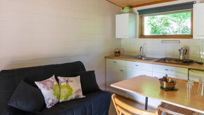 Een kleine keuken met een houten tafel en stoelen, een inbouwfornuis en een raam boven de spoelbak.