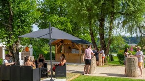 Een terras met tafels en stoelen, een overdekte pergola en een houten gebouw op de achtergrond.