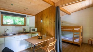Een compact vakantiehuisje met een kitchenette, een eethoek, een stapelbed en een raam met uitzicht op groen.