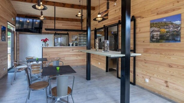 Een modern interieur met houten wanden, een eethoek met metalen stoelen, een keuken met een koelkast, en een schilderij aan de muur.