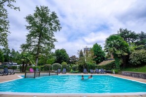 Una piscina con sillones de descanso y una valla, rodeada de árboles y follaje.