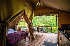 Um quarto com tenda, uma cama, uma mesa, cadeiras e vista para o verde.
