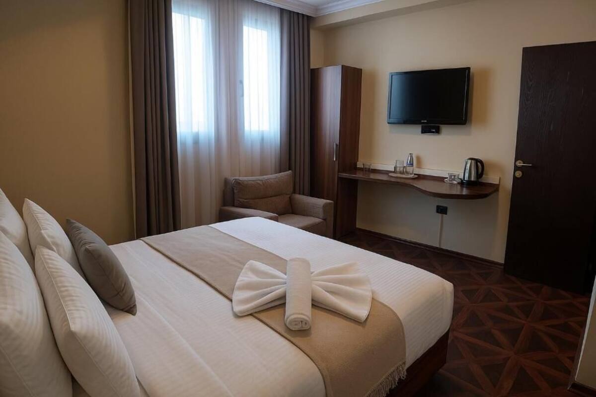 A hotel room with a large bed, a sofa, a TV, and a small table with a kettle and glasses.