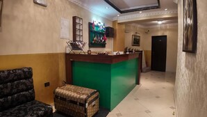 A reception area with a green counter, a patterned sofa, and a vintage suitcase. - Hotel Shadervan (Prizren)