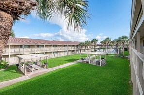 A hotel courtyard with a pool, covered seating areas, and a well-maintained lawn.