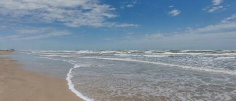 A beach with waves gently lapping onto the shore under a clear sky.
