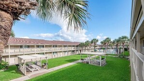 A hotel courtyard with a pool, covered seating areas, and a well-maintained lawn.