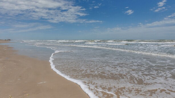 A beach with waves gently lapping onto the shore under a clear sky.