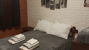 Una cama bien hecha con almohadas y toallas dobladas, una pared de ladrillo y una ventana con persianas.