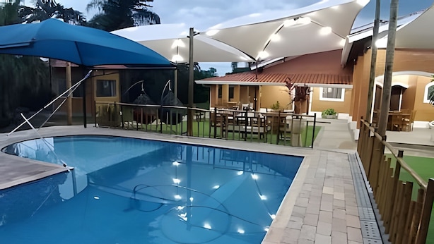 Una piscina con solárium de baldosas, sombrillas y mobiliario exterior.