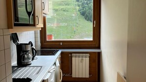 Eine kleine Küche mit Holzausstattung, einer integrierten Mikrowelle, einer Kaffeemaschine und Blick auf eine grüne Landschaft durch ein Fenster.