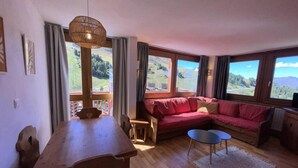 Ein gemütliches Wohnzimmer mit Holzesstisch, rotem Sofa und großen Fenstern mit schöner Aussicht.