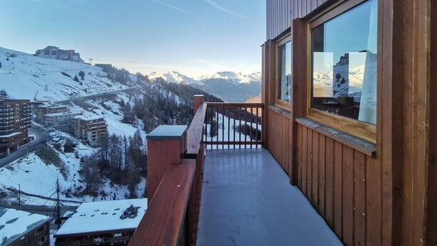 Ein Holzbalkon mit Blick auf verschneite Berge und Gebäude.
