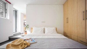 Ein modernes Schlafzimmer mit einem großen Bett, einem Holzschrank und einem kleinen Nachttisch mit einer Pflanze.