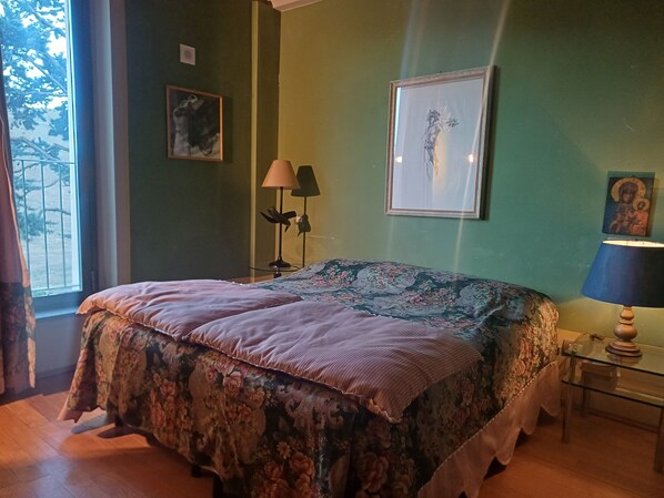 Un dormitorio con cama, mesita de noche, lámpara y ventana con cortinas.