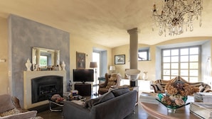 A living room with a fireplace, a sofa, a television, and a chandelier.