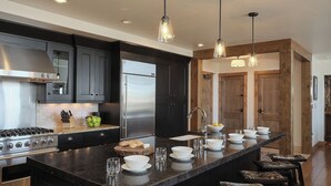 A modern kitchen with dark cabinetry, stainless steel appliances, and a central island with seating. - Luxury + Pool + Ski-in/Ski-out - Nightfall Ridge (Steamboat Springs)
