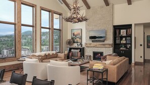 A spacious living room with a fireplace, large windows, and a stone wall. - Luxury + Pool + Ski-in/Ski-out - Nightfall Ridge (Steamboat Springs)