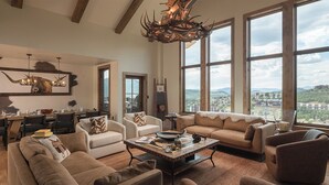 A spacious living room with a large window offering a city view, a chandelier, and a dining area with a table set for four. - Luxury + Pool + Ski-in/Ski-out - Nightfall Ridge (Steamboat Springs)