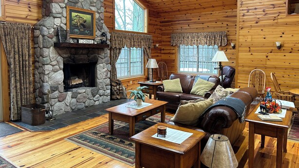 Un intérieur chaleureux de chalet avec une cheminée en pierre, des murs en bois, un canapé en cuir et un coin repas.