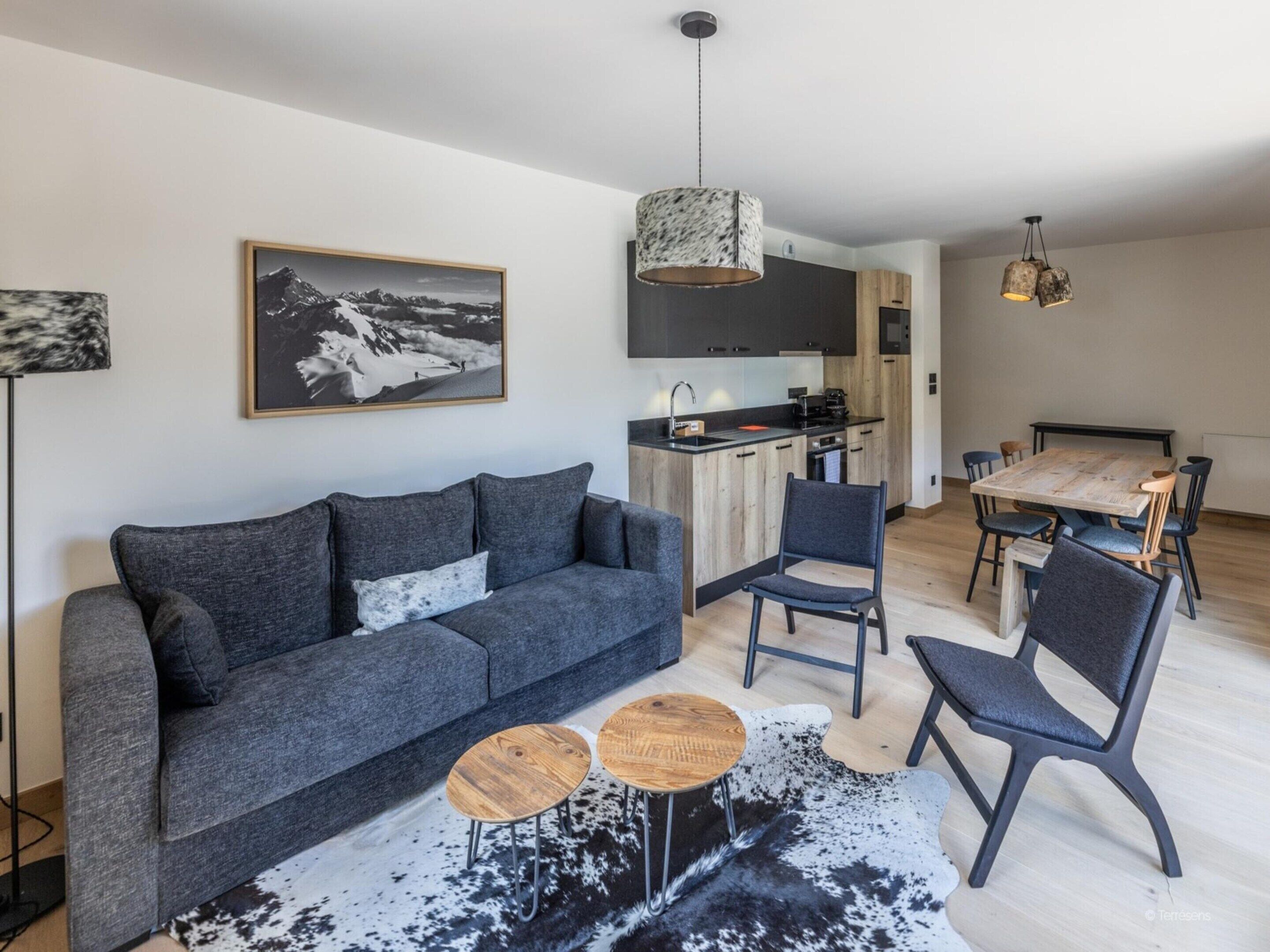 Een moderne woonkamer met een grijze bank, twee houten bijzettafels en een koehuidkleed.