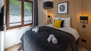 Ein Schlafzimmer mit einem großen Bett, einem Fenster mit Vorhängen, einer Wandlampe und einem gerahmten Bild.