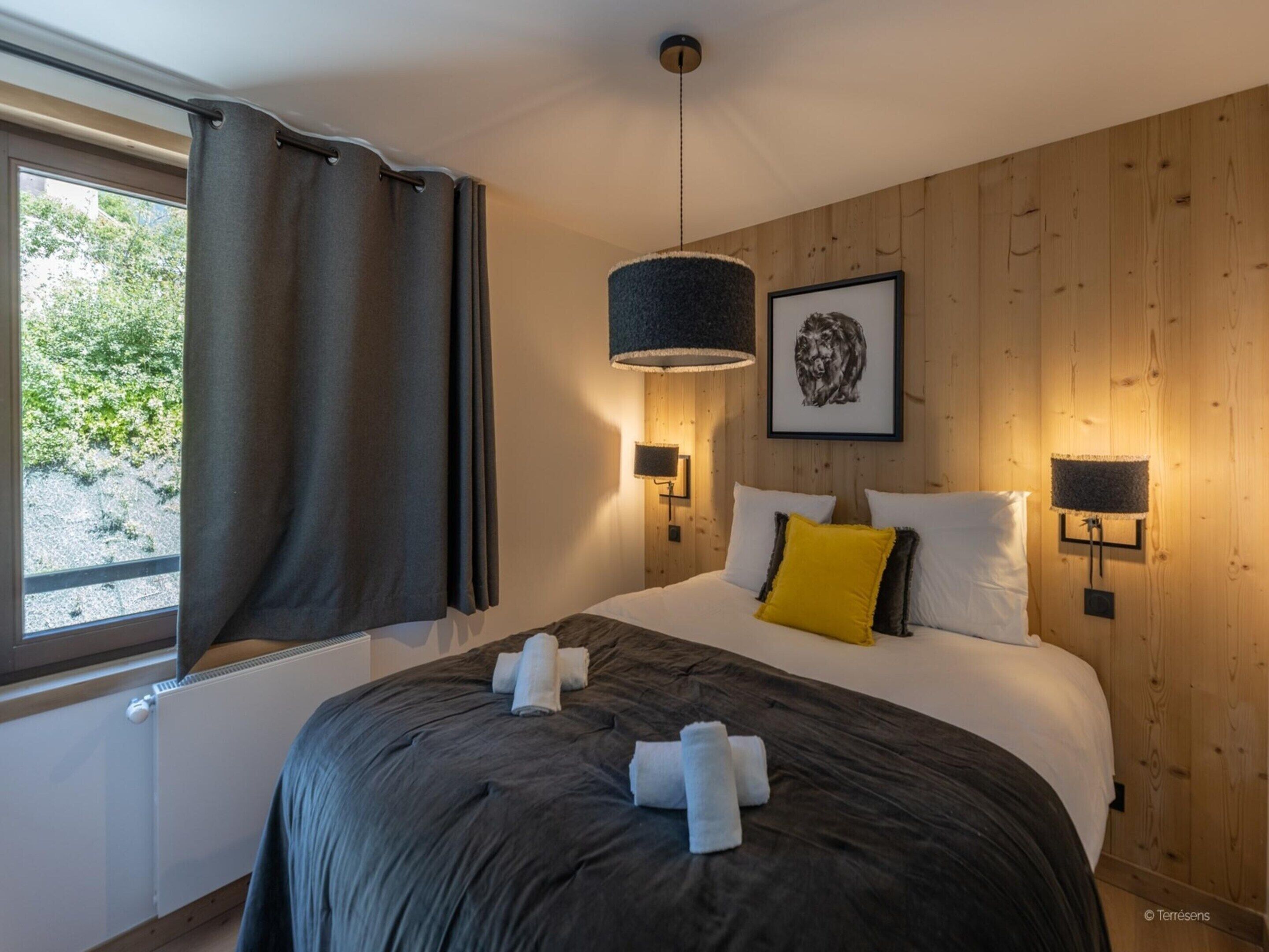 Une chambre à coucher avec un grand lit, des rideaux foncés, un tableau encadré au mur et deux lampes fixées au mur.
