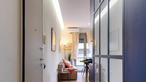A narrow hallway with a wooden floor leading to a seating area with a table and chairs.