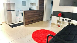 A modern living room with a black sofa, a red rug, and a kitchen area with white cabinets and appliances. - Charming Getaway with WiFi, AC in delightful Fort Lauderdale (Fort Lauderdale)
