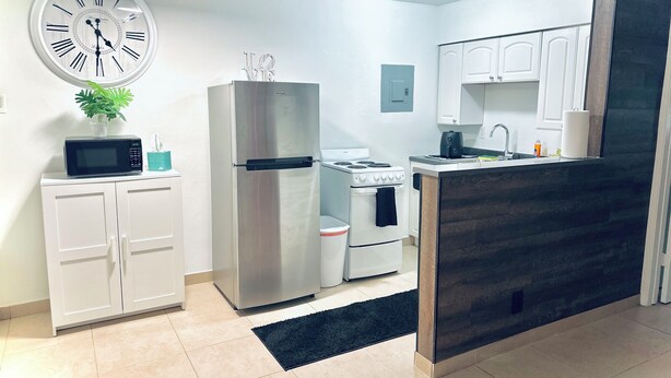 A modern kitchen with white cabinets, a stainless steel refrigerator, a microwave, a stove, and a clock on the wall. - Charming Getaway with WiFi, AC in delightful Fort Lauderdale (Fort Lauderdale)