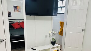 A room with a bed, a TV mounted on the wall, a shelf with towels, and a door. - Charming Getaway with WiFi, AC in delightful Fort Lauderdale (Fort Lauderdale)