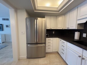 Una cocina moderna con armarios blancos, un refrigerador de acero inoxidable y una encimera negra.