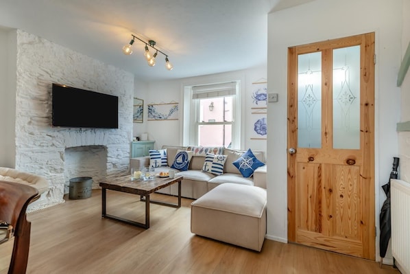 A living room with a stone wall, a sofa with nautical-themed cushions, a wooden coffee table, and a television mounted on the wall.