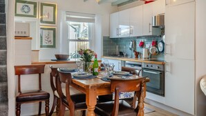 A modern kitchen with white cabinets, a dining table set for four, and a large window providing natural light. - 3 Bed in Brixham (oc-p30777) (Brixham)