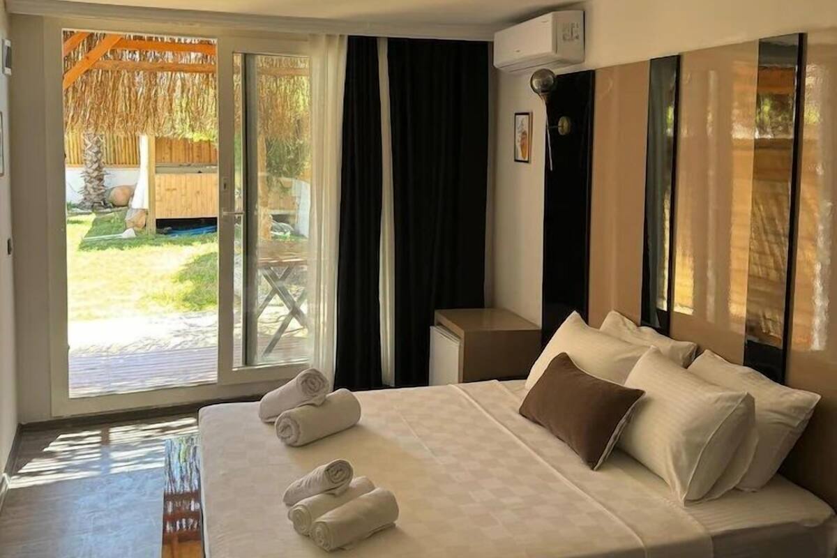 A hotel room with a bed, a small table, a chair, and a sliding glass door leading to an outdoor area.