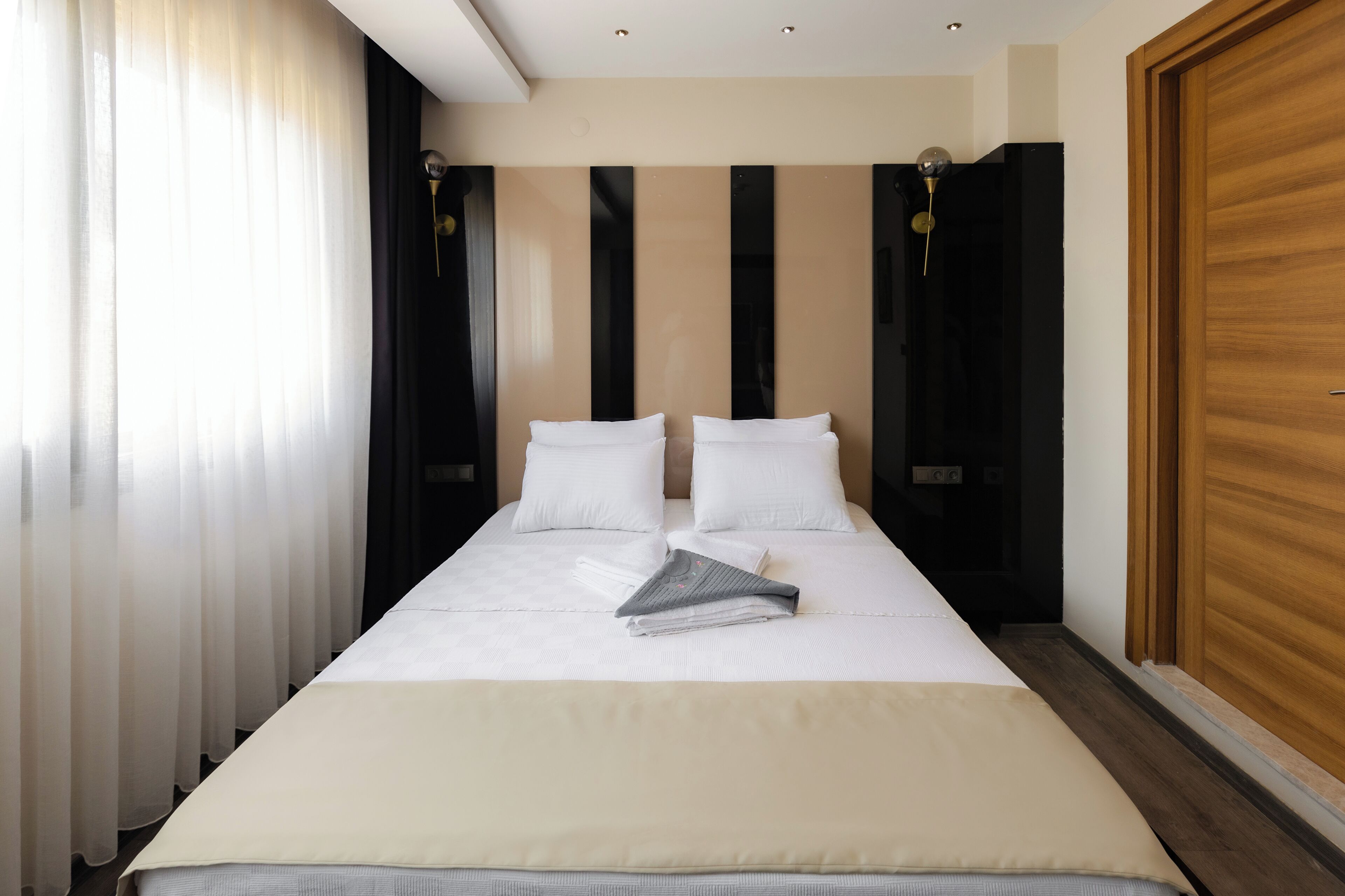A neatly made bed with white linens and a folded towel, a bedside table with a lamp, and a wooden door.