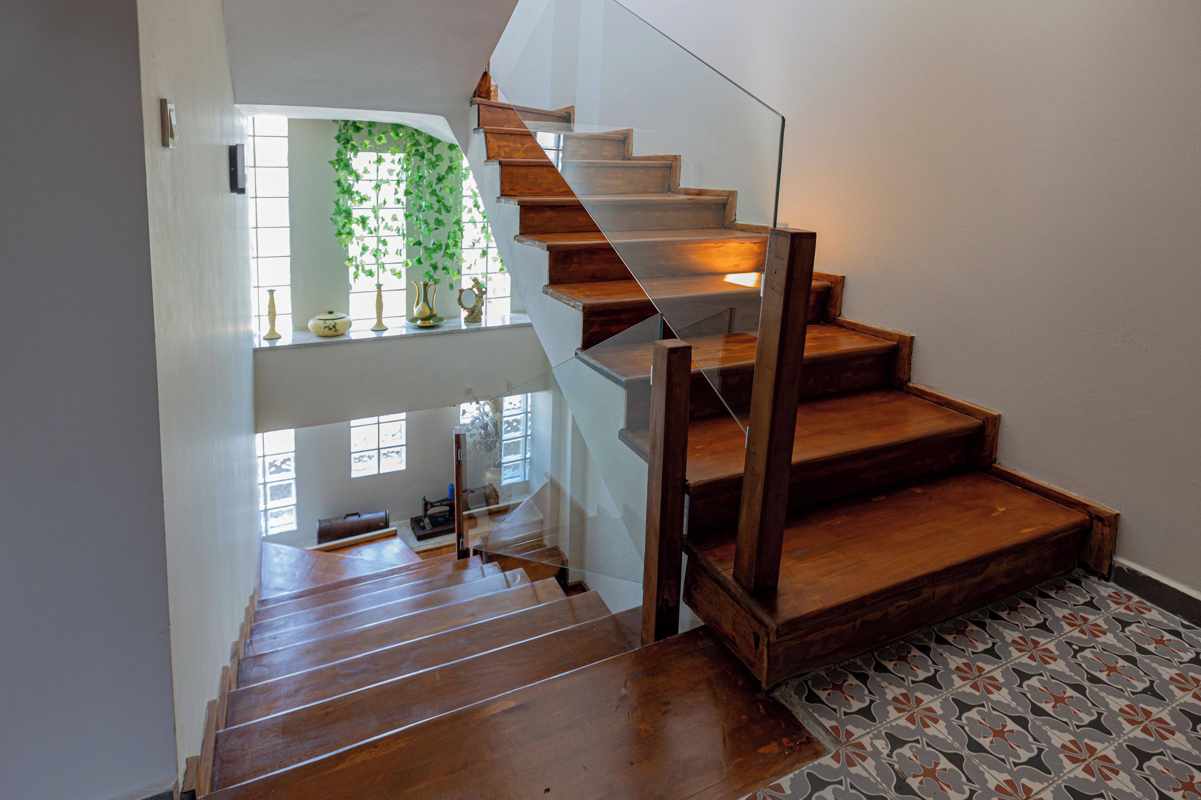 Un escalier en bois avec des rampes en verre menant à un palier doté d’une fenêtre et d’une plante.