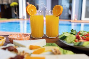 Two tall glasses of orange juice with straws and orange slices, a plate of salad, and a bowl of dip on a wooden table by a pool. - Mistral Alaçatı Hotel (Çesme)