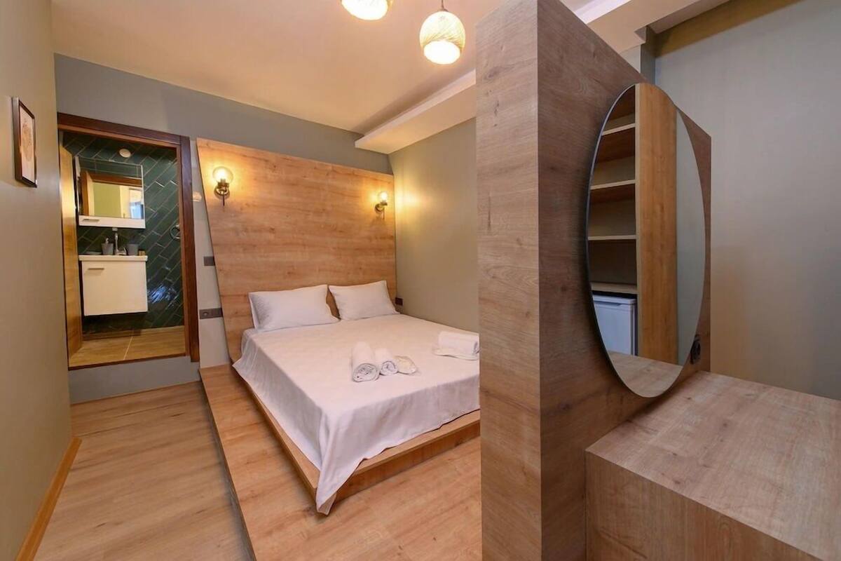 A modern hotel room with a wooden headboard, a large mirror, and a built-in shelf.