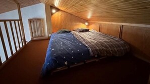 A bedroom with a wooden sloped ceiling, a bed with a star-patterned bedspread, and a nightstand. - 200m from resort center, view forest, terrace, balcony, fireplace or stove, tv, 42m², La Plagne (La Plagne)