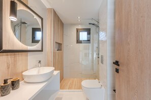 A modern bathroom with a large oval sink, a mirror, a shower enclosure, and a toilet.