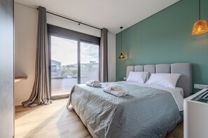 A modern bedroom with a large bed, a view through a sliding door, and a pendant light.