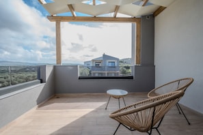 A balcony with a view of a house, a round table, and two wicker chairs.