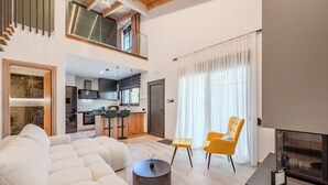 Un salon moderne avec un canapé, deux fauteuils, une table basse, une cheminée et une cuisine en arrière-plan.